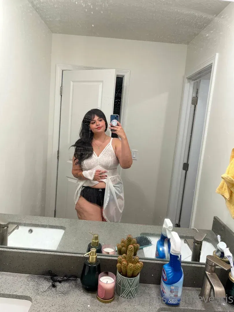 Eve Iris in einem weißen Camisole und Morgenmantel beim Spiegel-Selfie im Badezimmer