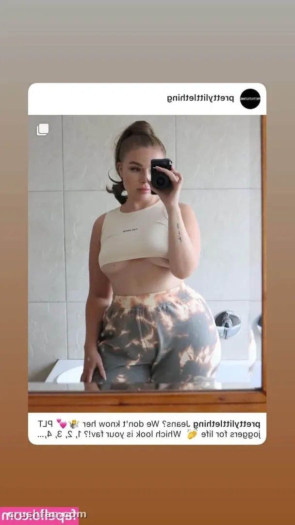 Emma Christina tomándose una selfie frente al espejo en un baño alicatado, con un top corto claro y pantalones estampados