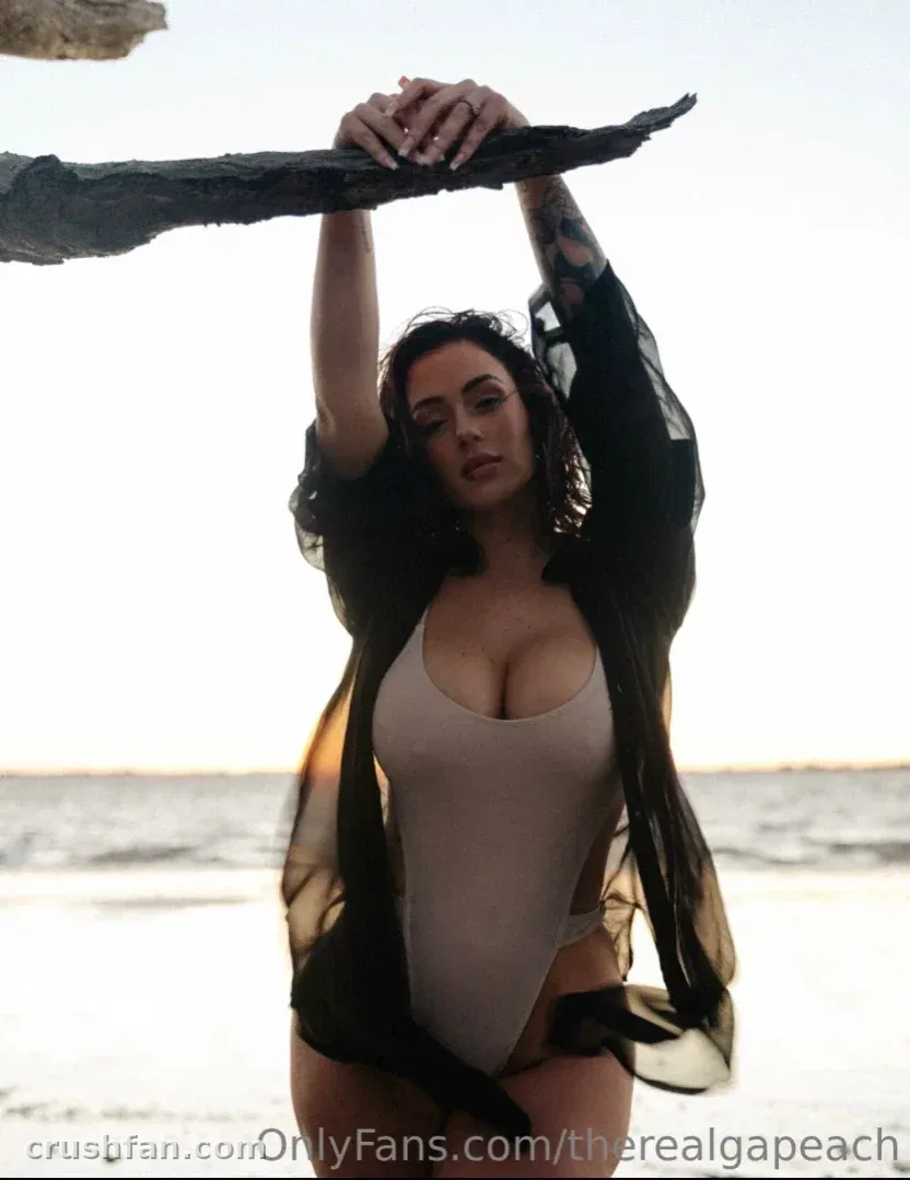 Mulher de maiô bege segurando tecido preto transparente acima da cabeça em uma praia