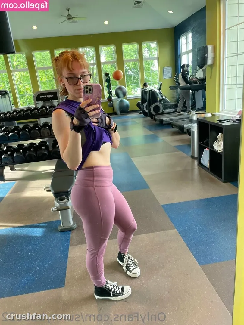 Woman in a purple crop top and mauve leggings taking a gym mirror selfie