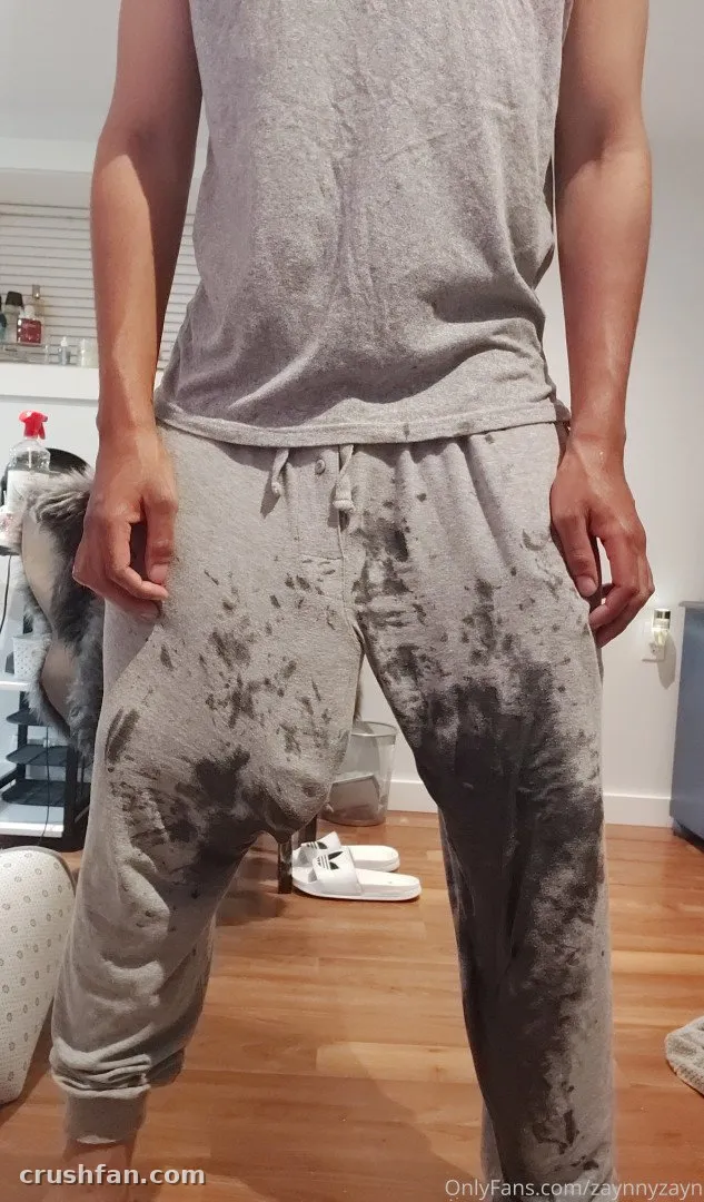 Creador con top sin mangas gris y joggers grises manchados de pie en interiores sobre suelo de madera