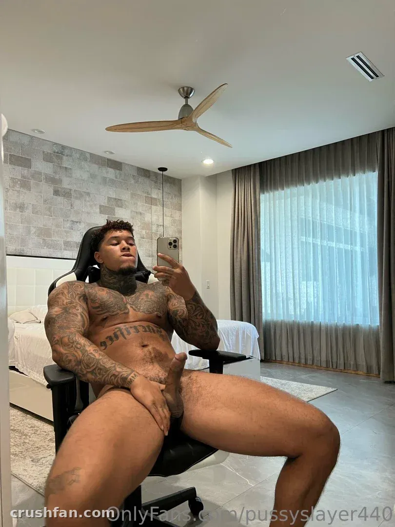 DOMINATOR sentado em uma cadeira preta tirando uma selfie no espelho em um quarto claro