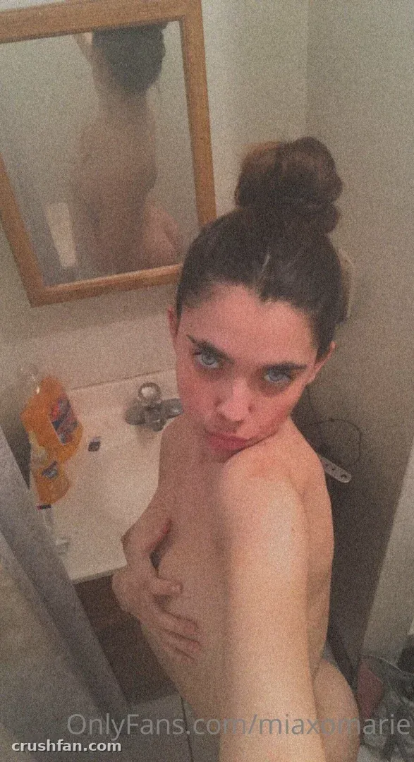 Mia Marie prenant un selfie devant le miroir dans une salle de bain avec un miroir à cadre en bois et un lavabo blanc.
