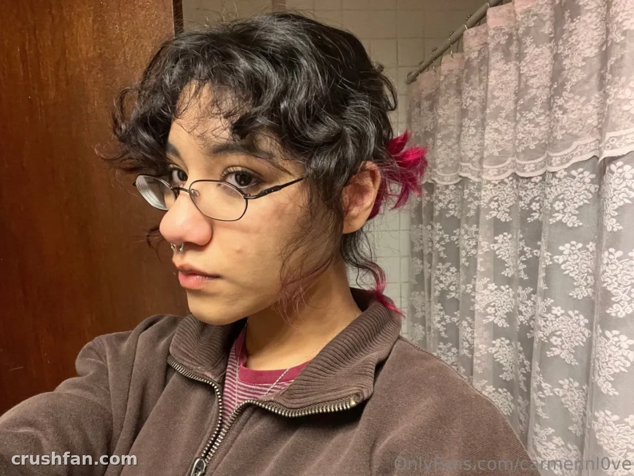 Official Carmen Love portant des lunettes et une veste marron dans un selfie de salle de bain.