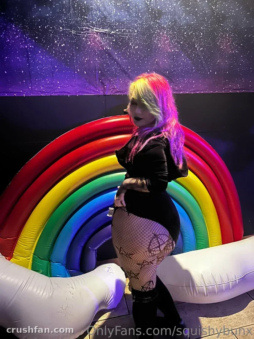 Brooke Ivy con blusa oscura y medias de rejilla posando junto a un arcoíris bajo luces estrelladas