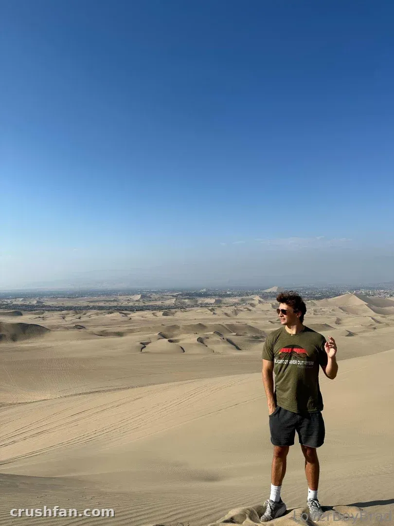 Leo standing on a desert dune wearing an olive t-shirt and sunglasses under a clear blue sky.