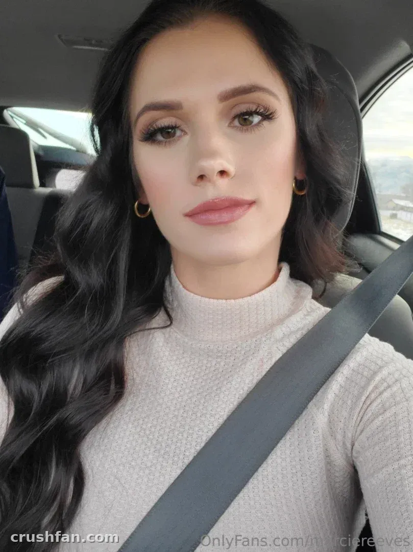 Marcie Reeves con un cuello alto beige sentada en un coche con un cinturón de seguridad cruzando su pecho