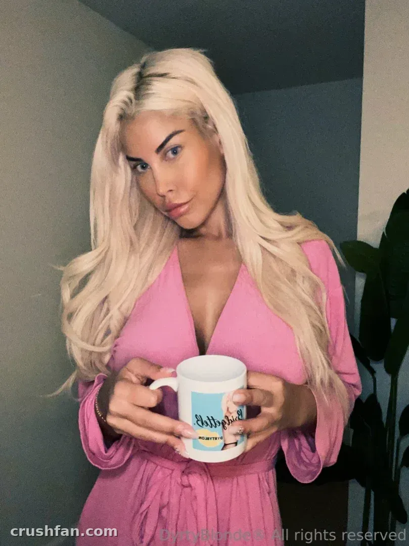 Bridgette B de roupão rosa segurando uma caneca branca em ambiente interno