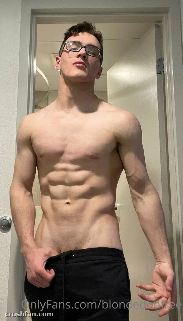 Homem sem camisa de calça preta e óculos tirando uma selfie no espelho em uma porta