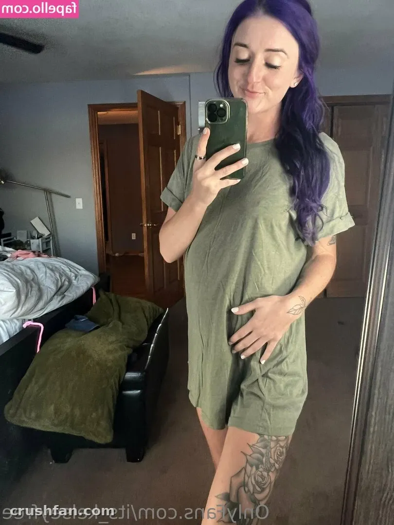 Kelsey Anne in einem olivfarbenen T-Shirt-Kleid, die in einem Schlafzimmer ein Spiegel-Selfie macht.