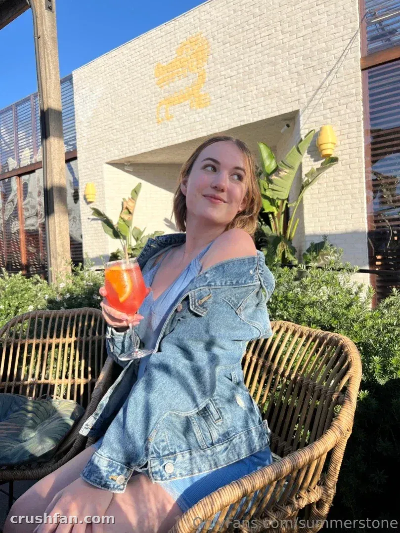 Summer sentada en una silla de ratán sosteniendo una bebida fría en un patio soleado
