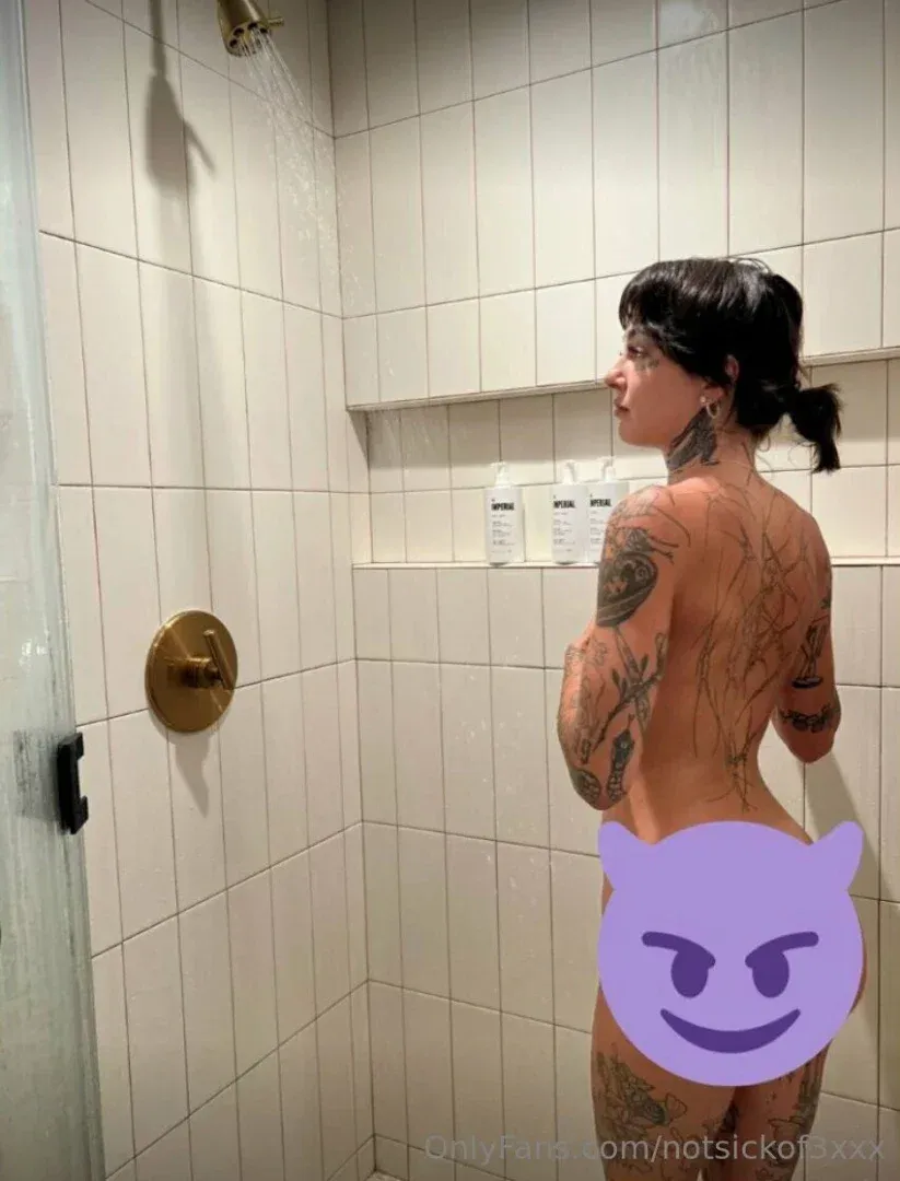 Keaton Belle standing in a white tiled shower under running water