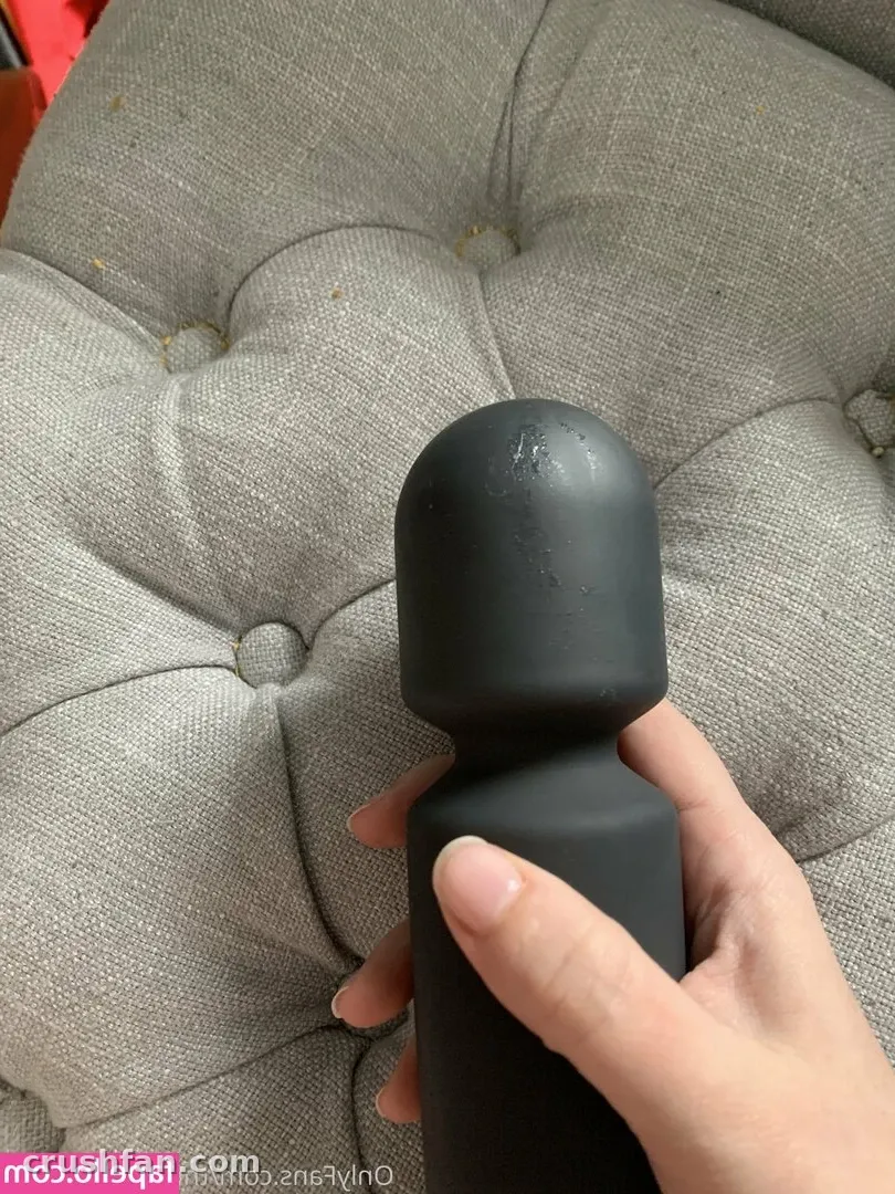 Nahaufnahme einer Hand, die einen mattschwarzen Gegenstand über einem grauen gepolsterten Sofakissen hält.