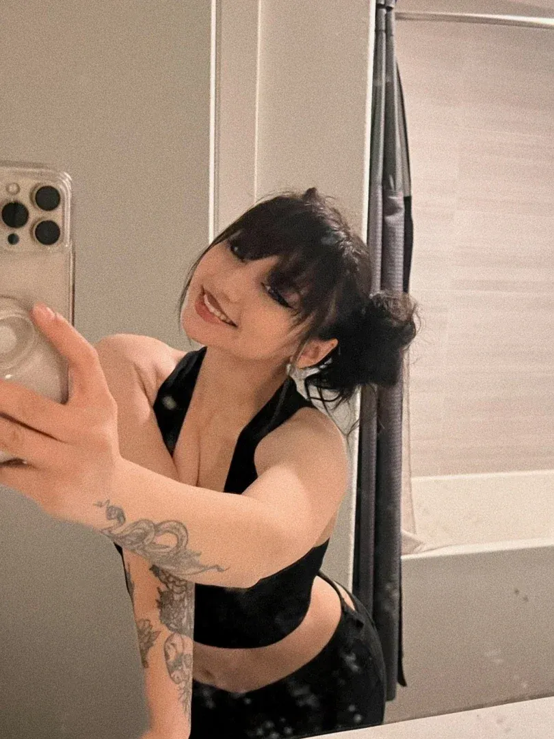 Jade in a black top taking a mirror selfie in a bathroom.