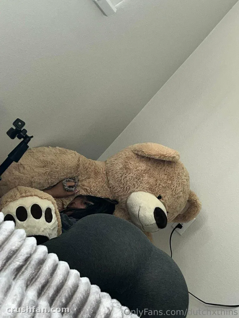 DutchxThins lying next to a large brown teddy bear on a bed indoors