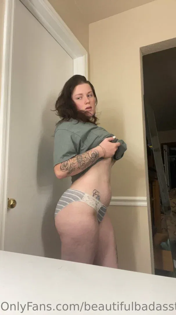 Jess en t-shirt gris et sous-vêtements rayés debout en intérieur près d'une porte blanche