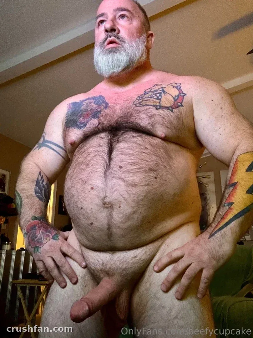 BeefyCupCake shirtless indoors with tattoos and a grey beard in warm light