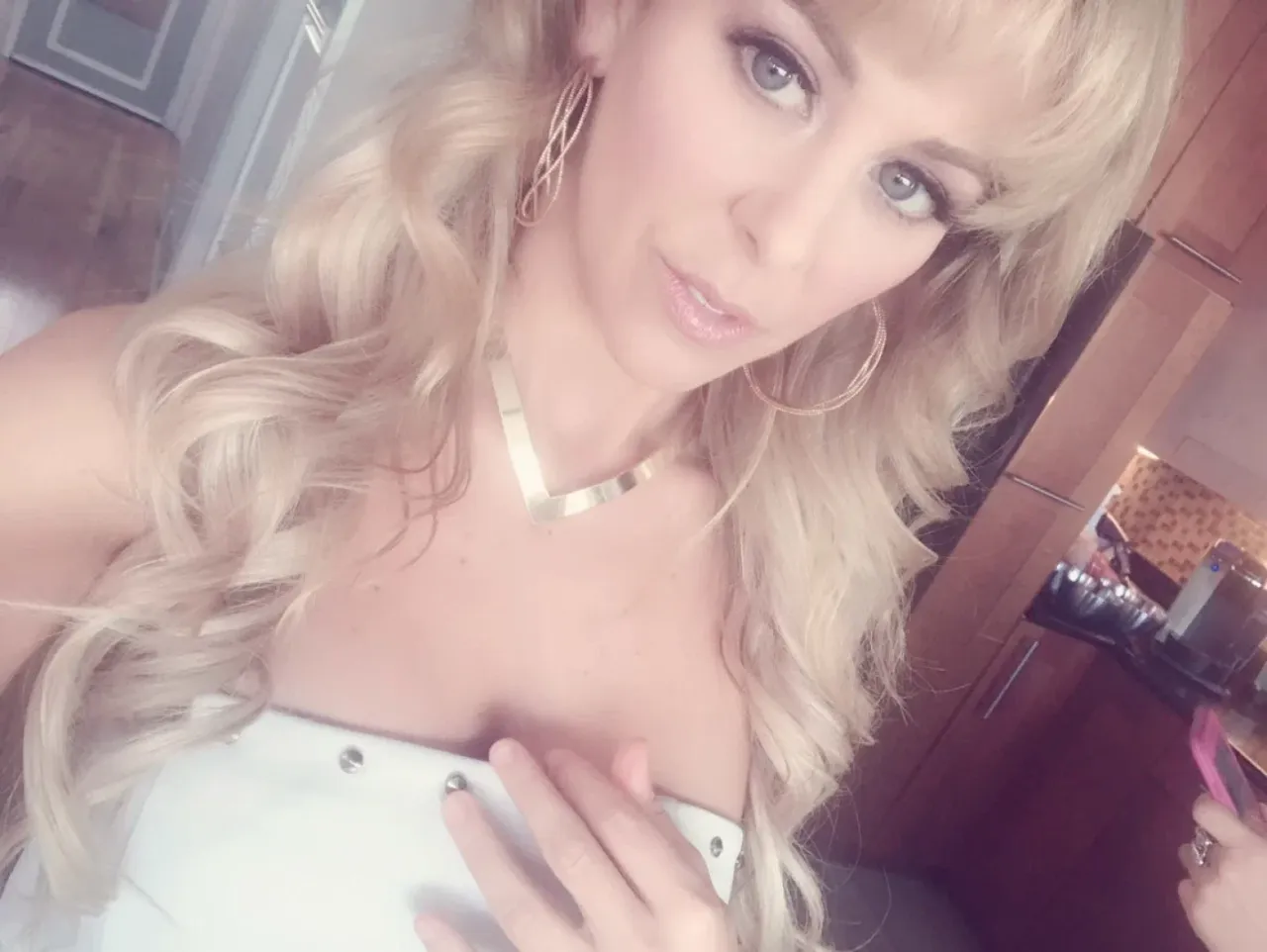 Cherie DeVille taking a close indoor selfie in a white studded top with gold jewellery