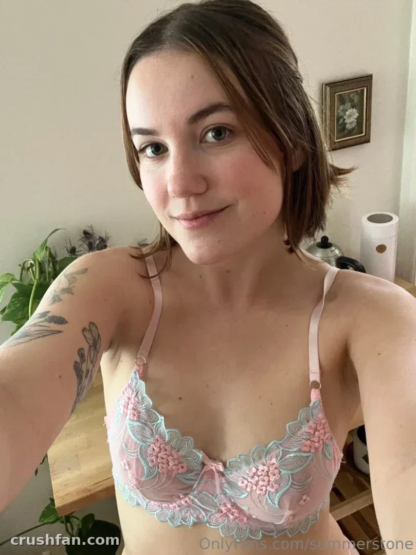 Summer in einem Pastell-Spitzen-BH, die drinnen ein Selfie macht, mit einer Pflanze hinter sich.