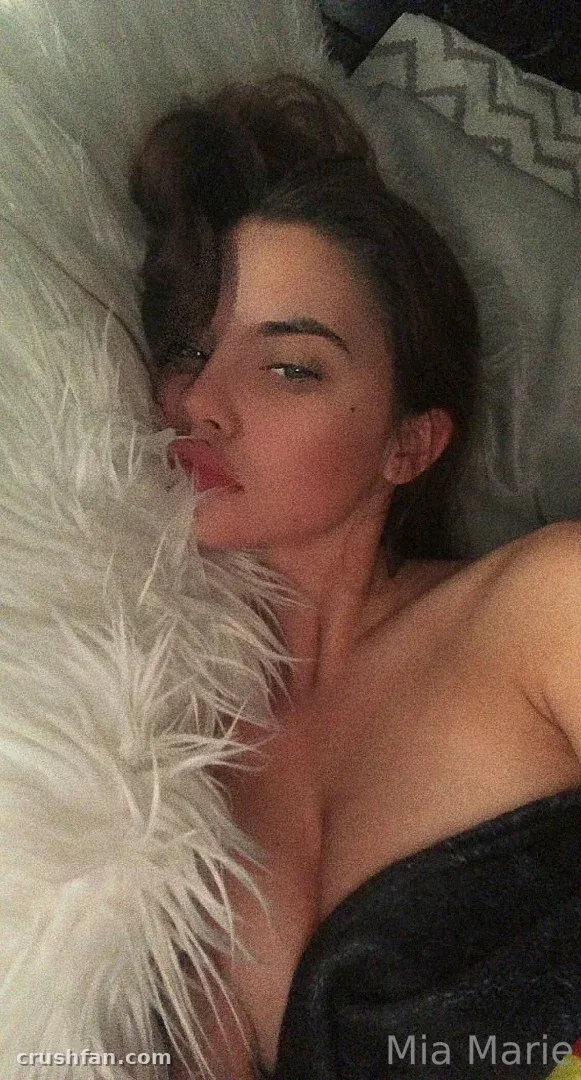 Mia Marie la tête posée sur un oreiller blanc duveteux dans une lumière chaude et tamisée