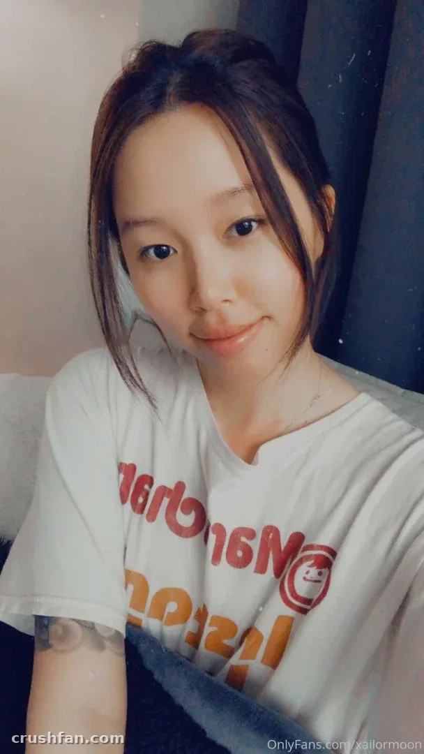 Creator in einem übergroßen weißen Grafik-T-Shirt, lächelnd in einem nahen Indoor-Selfie.