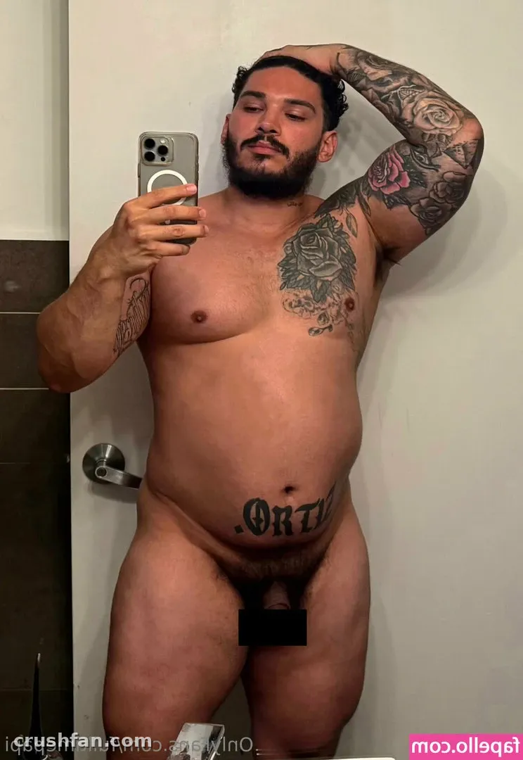 Diego Grant taking a mirror selfie in a bathroom, showing chest and arm tattoos