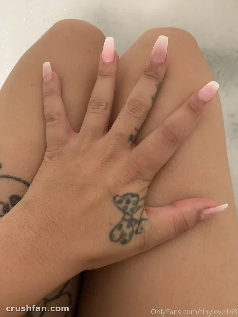 Primer plano de las manos de una mujer con uñas manicuradas rosas y un tatuaje de mariposa descansando sobre su regazo.