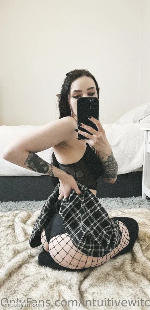 Creator in a black top and plaid shirt taking a mirror selfie while sitting on a rug.