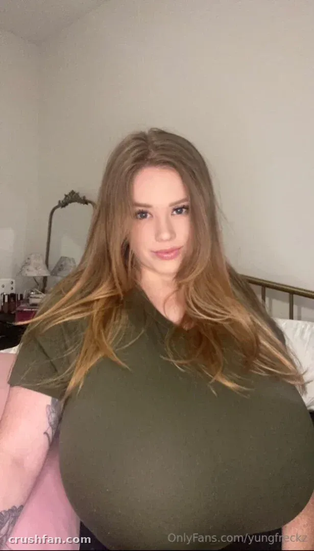 Missy em uma camiseta verde-oliva posando em ambiente interno em uma sala com luz suave