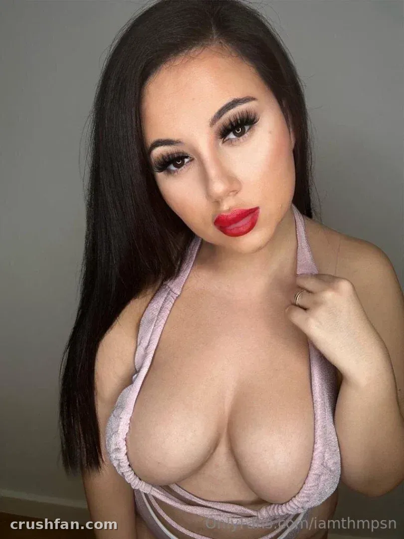 THMPSN in a pink halter top against a grey wall, wearing red lipstick