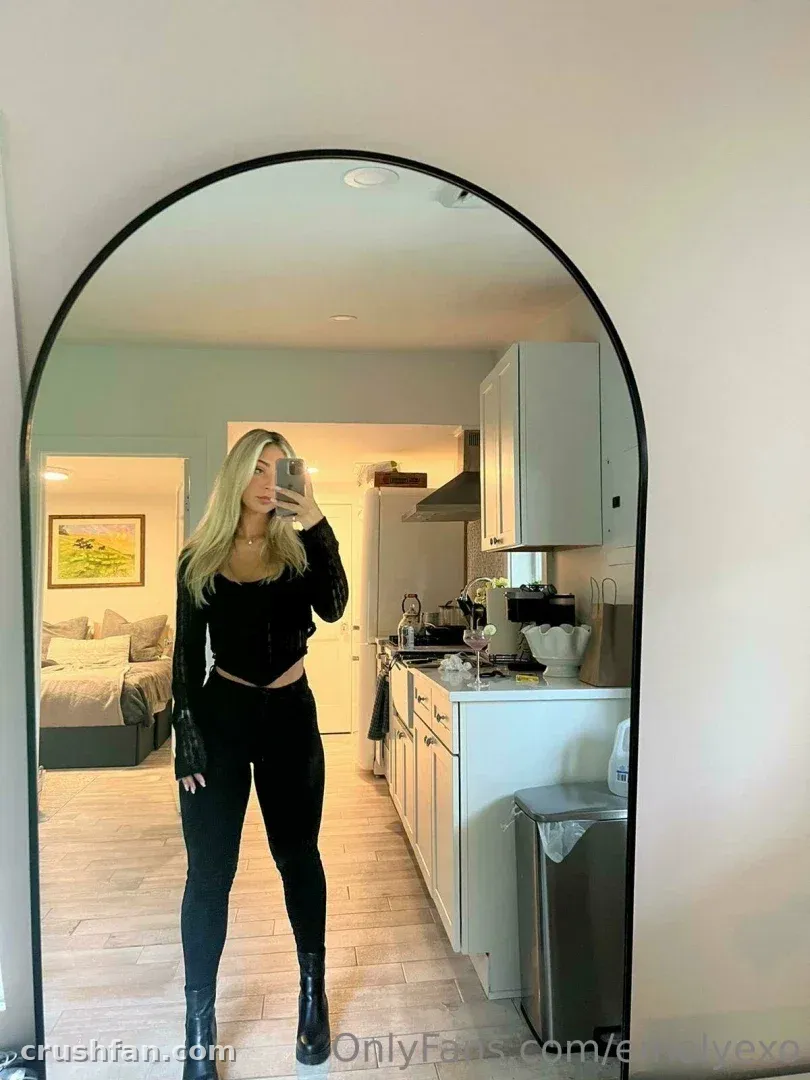 Em tirando uma selfie no espelho com um look preto dentro de uma cozinha clara.