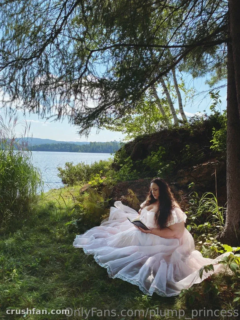 Criadora em um vestido de tule branco lendo ao lado de um lago sob galhos pendentes