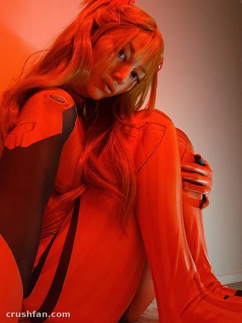 Alice NZ seated in a red bodysuit against a plain wall under warm red light