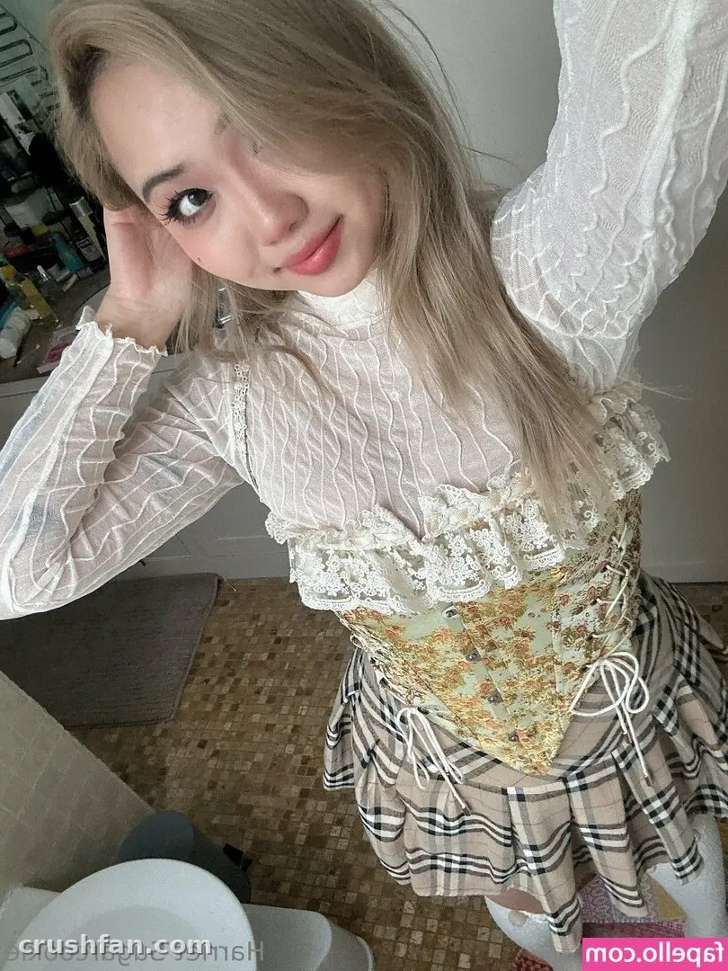 Creator in a white lace top and plaid skirt tilting her head indoors