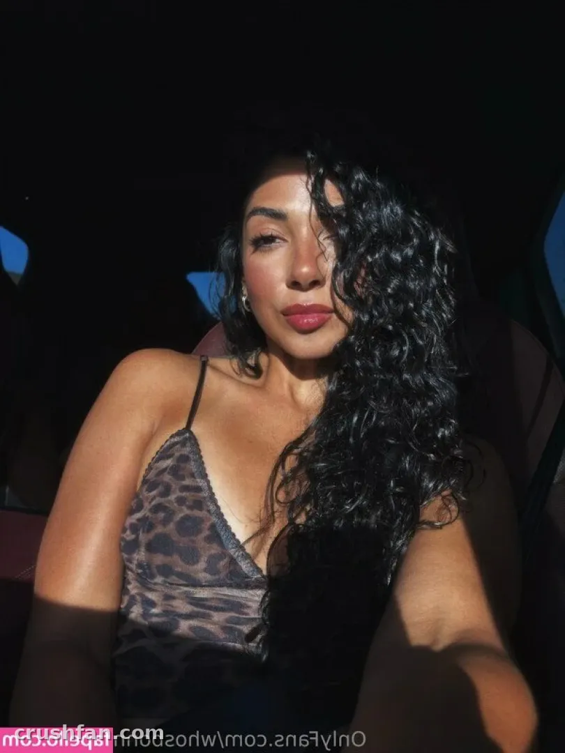 Creator in a leopard-print camisole and curly hair, photographed in dim lighting against a dark background.