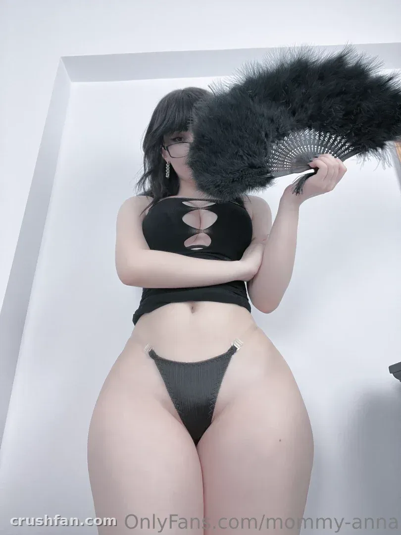 Anna en haut et bas noirs à découpes tenant un grand éventail noir en plumes dans un studio blanc