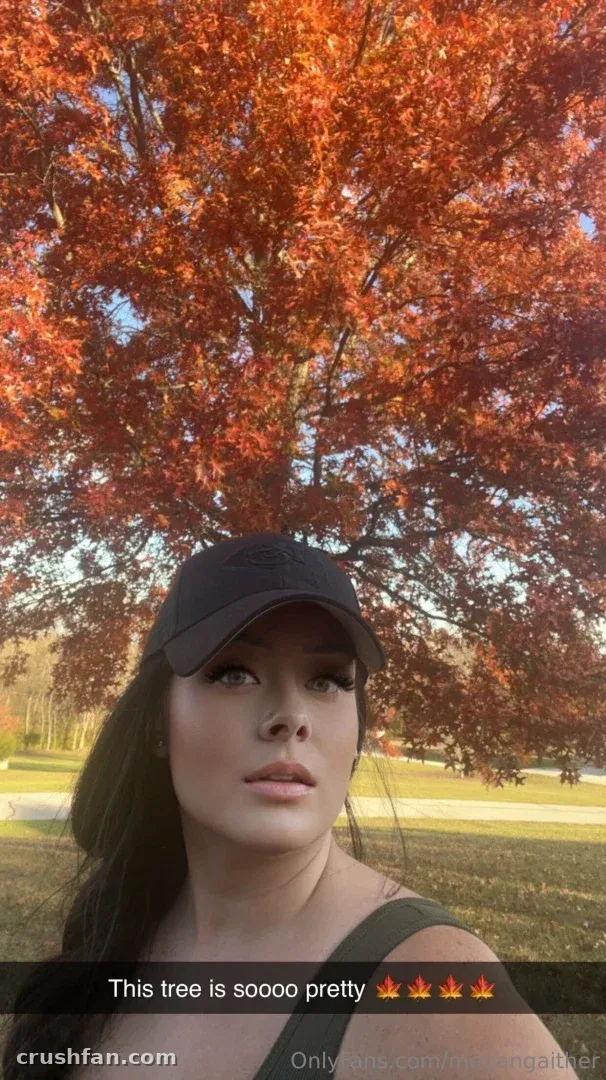 Woman in a dark cap standing under a tree with red autumn leaves