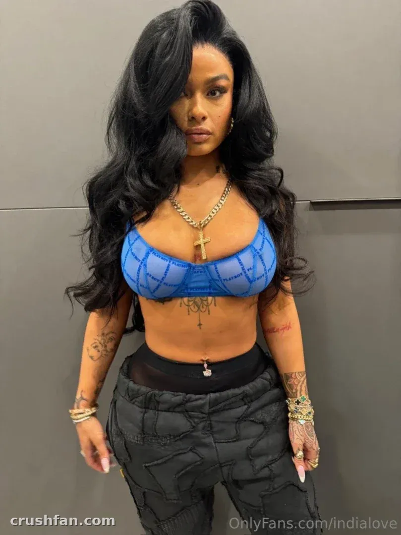 India Love in einem blauen Mesh-Crop-Top und dunkler Cargohose vor einer grauen Wand