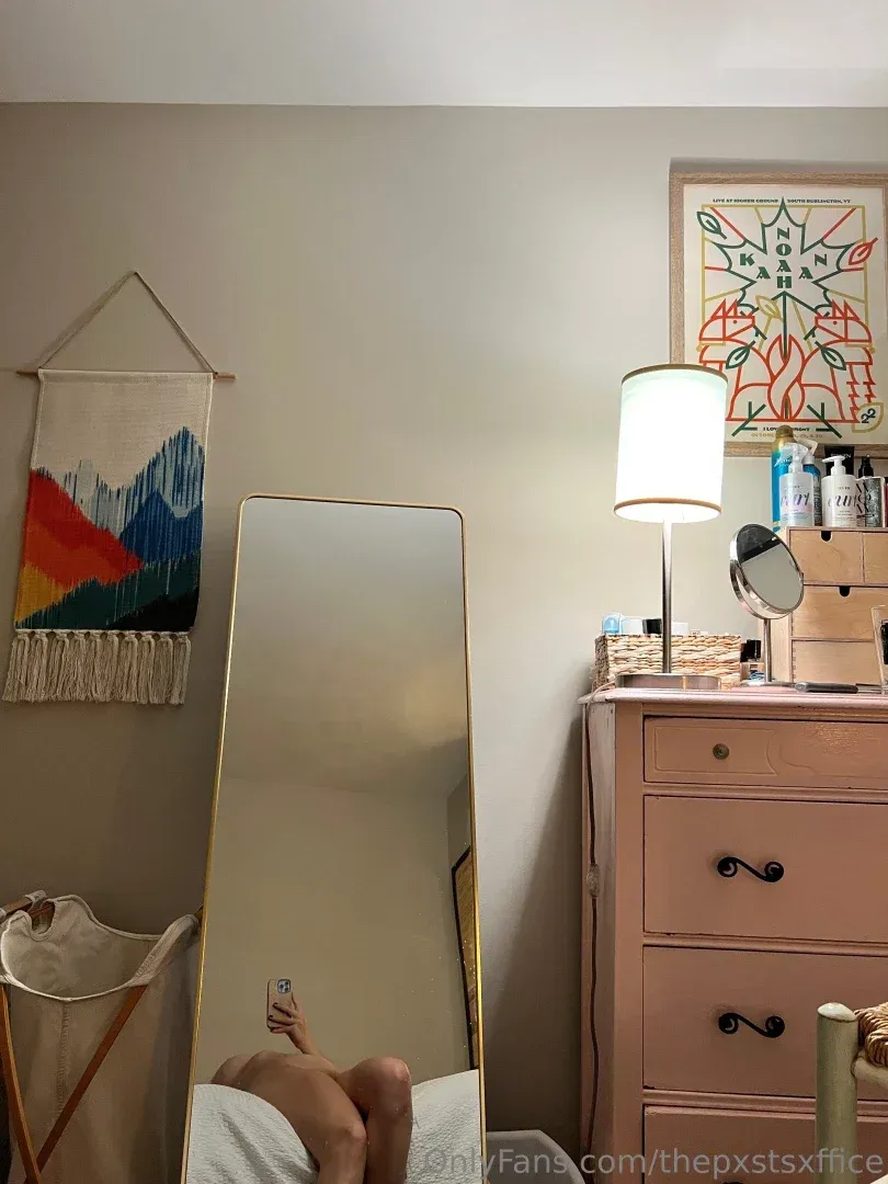 Selfie de espelho em um quarto com tapeçaria de parede tecida e uma cômoda rosa.