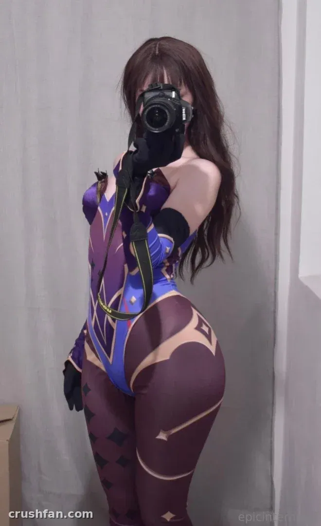 Anna dans un bodysuit cosplay violet et bleu tenant un appareil photo devant un fond blanc.