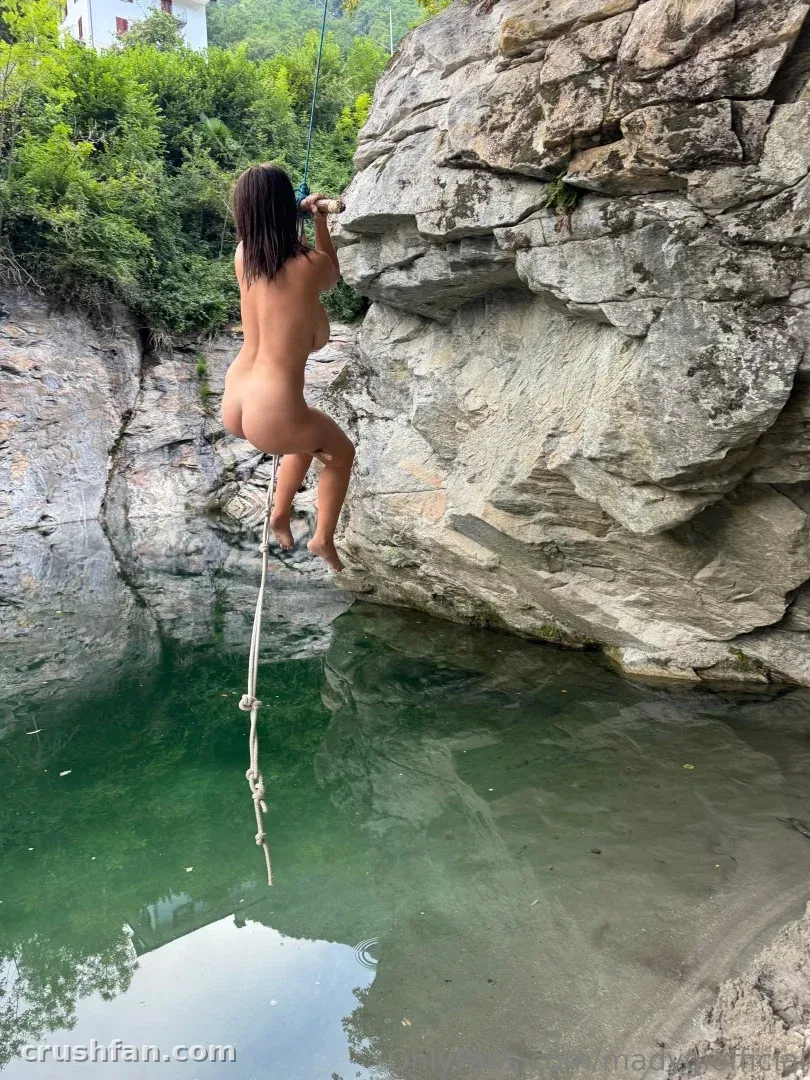 Mady_Gio swinging on a rope above a green river pool surrounded by rocks and trees