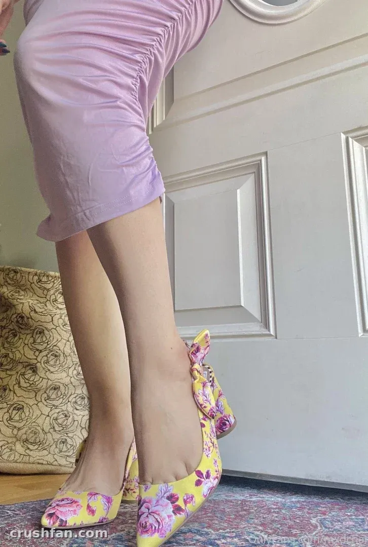 Kajol con pantalones lila y tacones amarillos florales de pie junto a una puerta blanca en interiores.