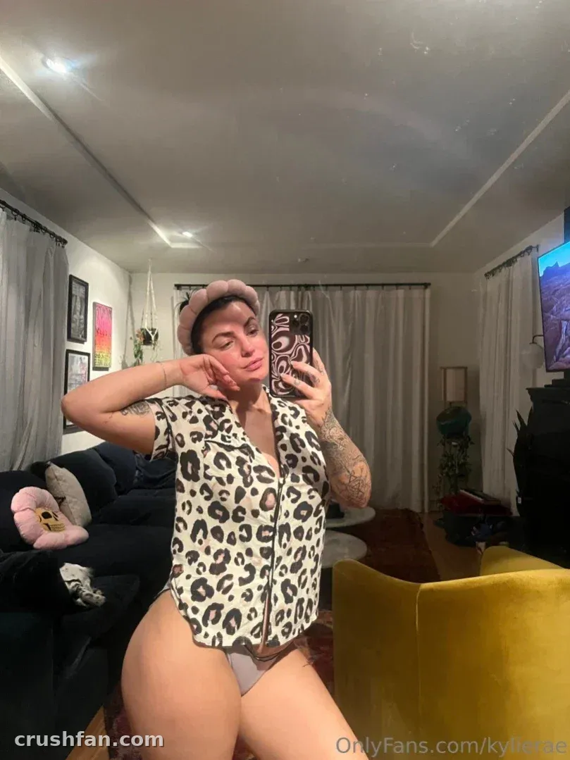 Kylie Rae tirando uma selfie no espelho com uma camisa de estampa de leopardo e calcinha cinza.