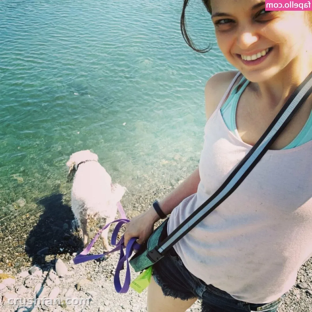 Creator in a tank top and denim shorts holding a purple leash beside clear water