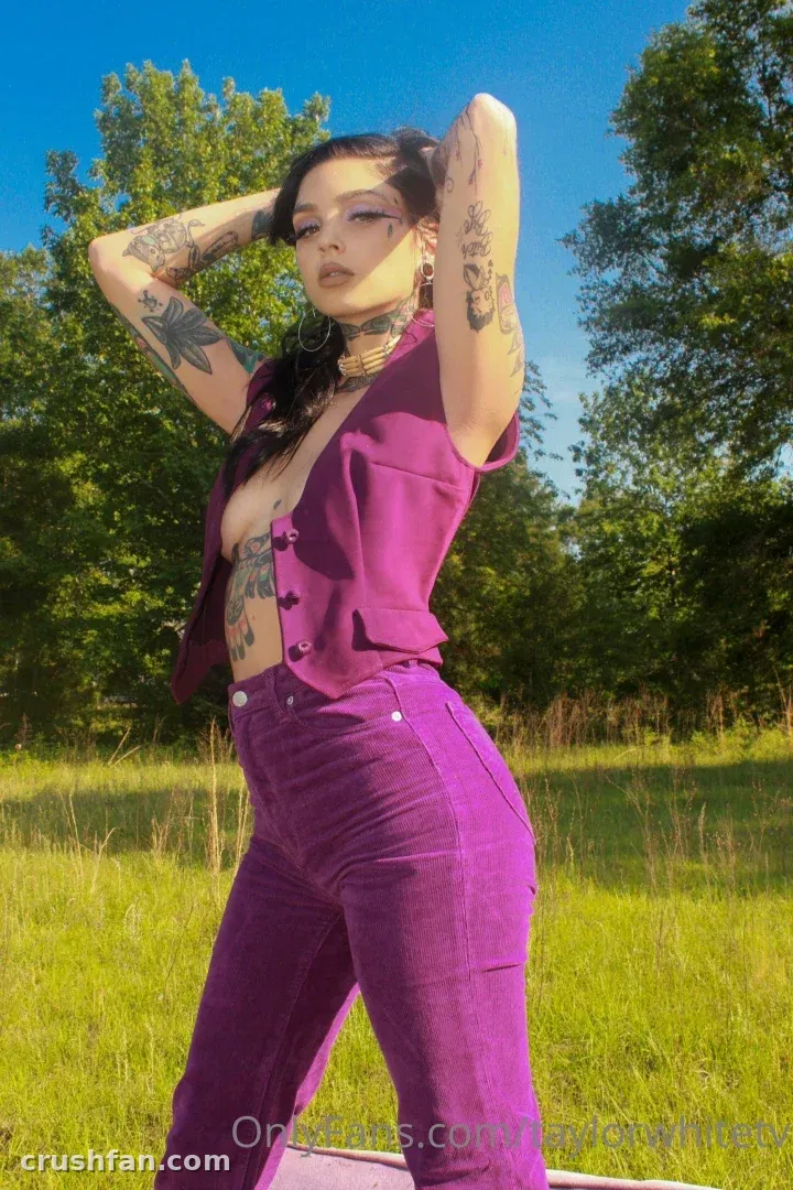 Taylor white com um colete roxo e jeans em pé em um prado ensolarado