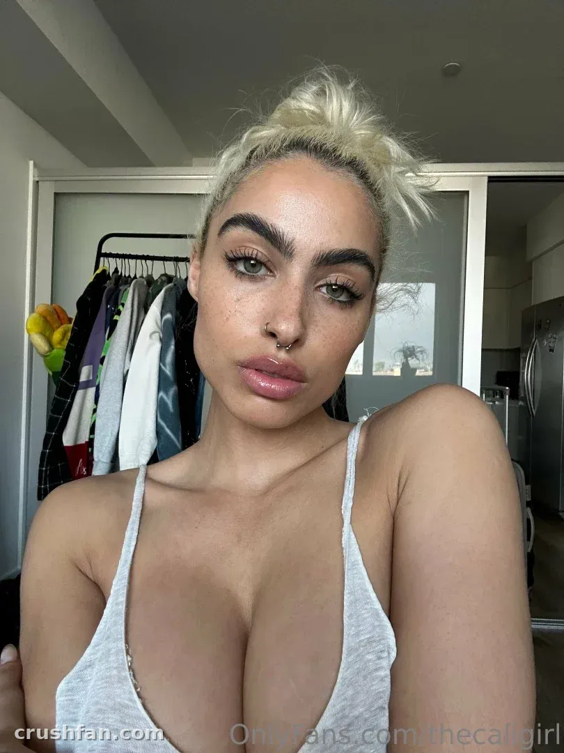 Thecaligirl prenant un selfie en gros plan en intérieur dans un haut gris clair.