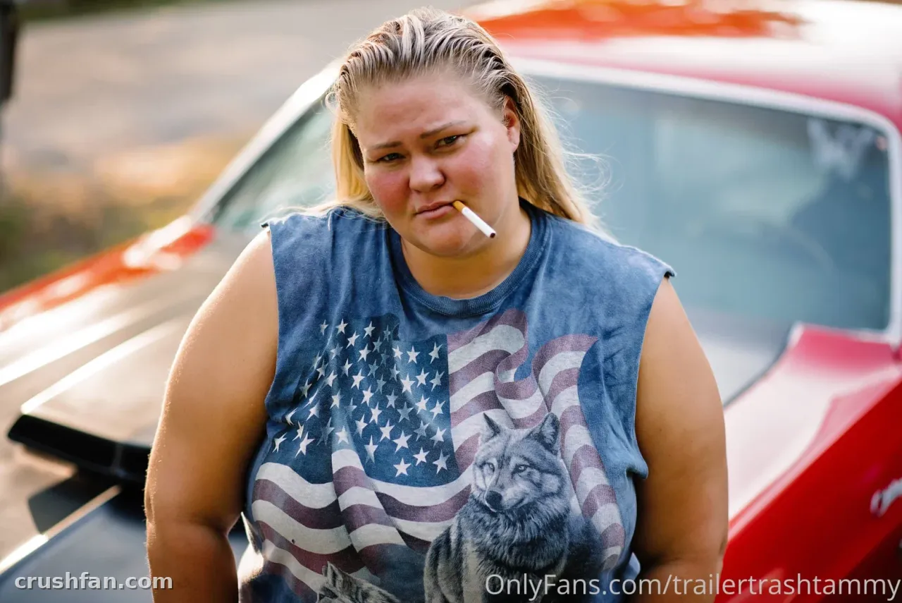 Chelcie Lynn in a sleeveless flag print top standing beside a red car outdoors