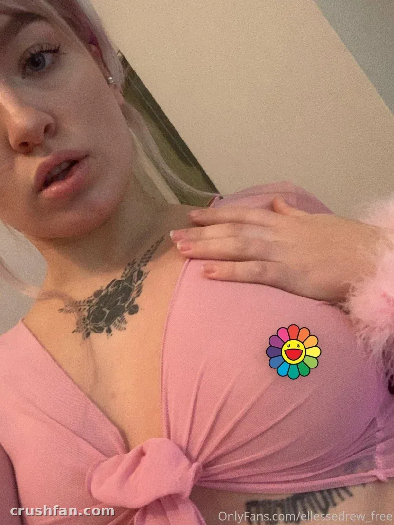 Close-up selfie of a woman in a pink knotted top with fluffy cuffs indoors