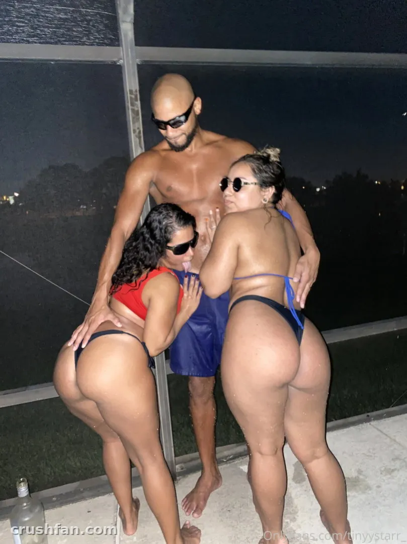 Woman in a red bikini standing on a patio by a pool at night with two other people.