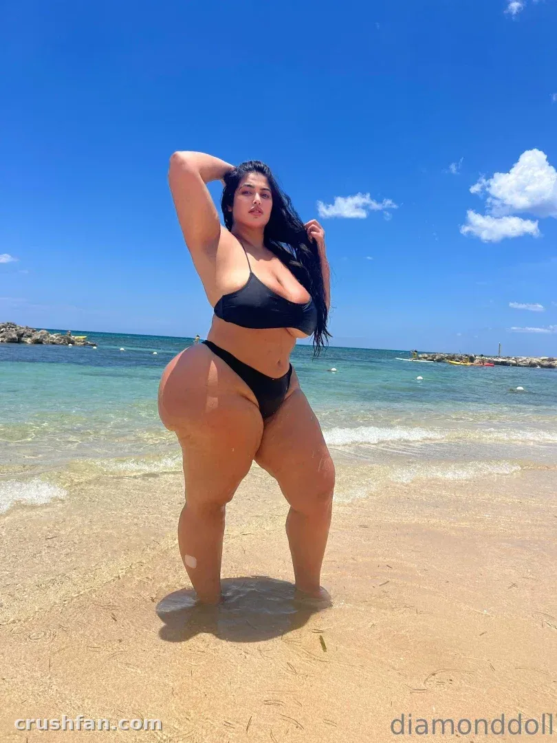 Diamonddoll in a black bikini standing in shallow water on a sunny beach